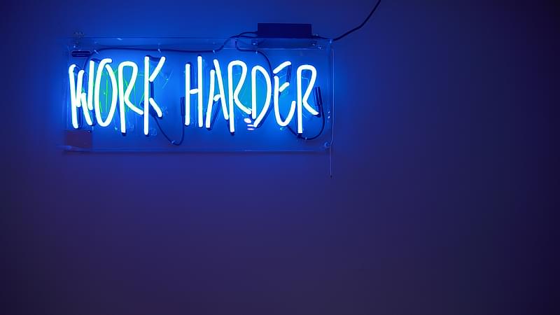A neon blue sign reading, "Work Harder"
